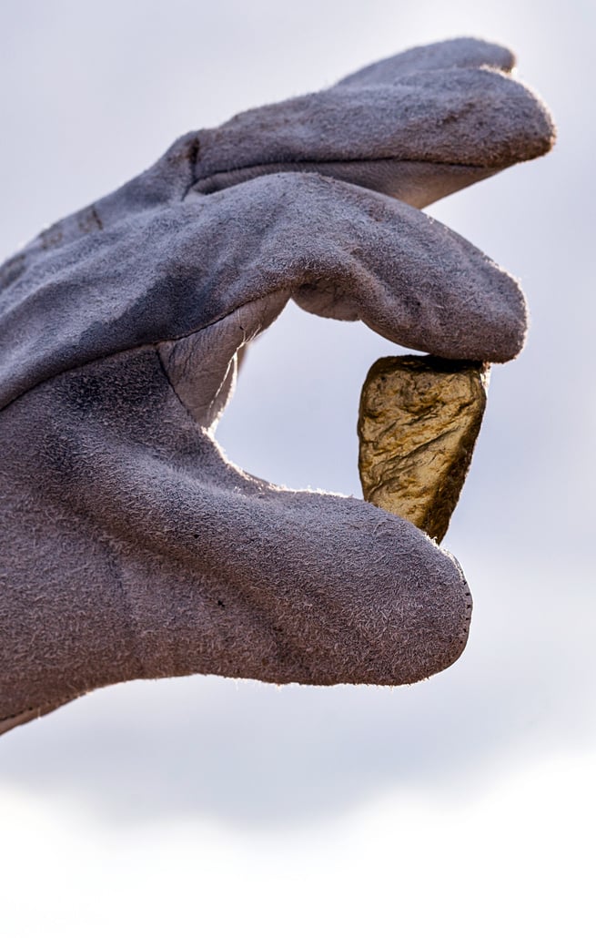 gold stone close-up in the hand of a mining company with glove. Mining exploration concept.